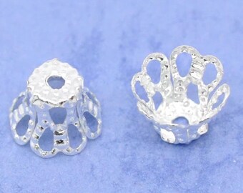 May include: Two silver metal bead caps with a decorative, openwork design. The caps have a round hole in the center and a scalloped edge.