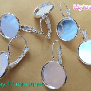 May include: Five silver earring settings with 12 mm round glass inserts. The settings are open on the back and have a lever back closure. The text "Tray 12 mm inner" is visible in the bottom left corner of the image.