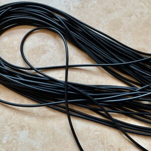 May include: A close-up of a large bundle of black elastic cord. The cord is tightly wound and appears to be made of a durable material.