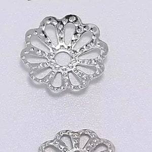 Op de afbeelding: Twee zilverkleurige metalen bloemvormige kralencaps, elk met een diameter van 9 mm. De kralencaps hebben een delicaat, ingewikkeld ontwerp met een ronde opening in het midden.