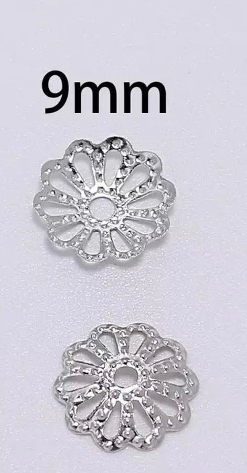 Op de afbeelding: Twee zilverkleurige metalen bloemvormige kralencaps, elk met een diameter van 9 mm. De kralencaps hebben een delicaat, ingewikkeld ontwerp met een ronde opening in het midden.