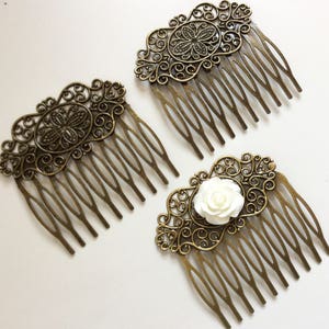 May include: Three antique bronze hair combs with ornate filigree designs. Two combs feature a central floral motif, while the third has a white rose accent. The combs have multiple tines for securing in hair.