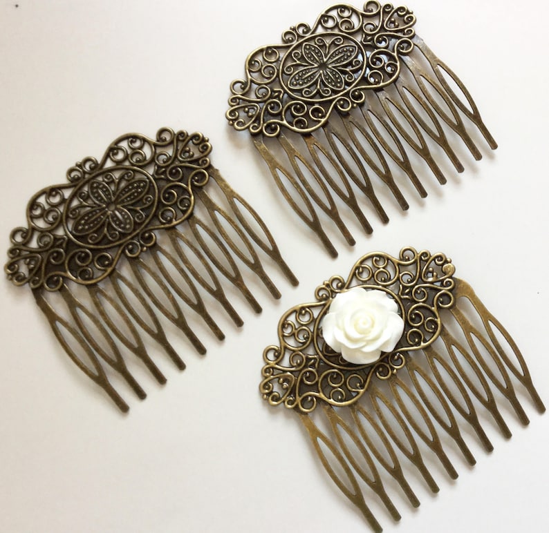 May include: Three antique bronze hair combs with ornate filigree designs. Two combs feature a central floral motif, while the third has a white rose accent. The combs have multiple tines for securing in hair.