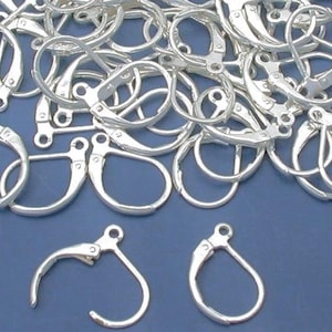 May include: A pile of silver-toned earring hooks, with two individual hooks in the foreground. The hooks are made of metal and have a spring-loaded clasp.