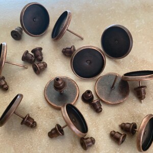 Puede incluir: Un conjunto de 12 monturas de pendientes de cobre antiguo con biseles redondos. Las monturas están diseñadas para sujetar cabujones redondos de 12 mm. Las monturas tienen un acabado de cobre oscuro y son perfectas para crear pendientes personalizados.