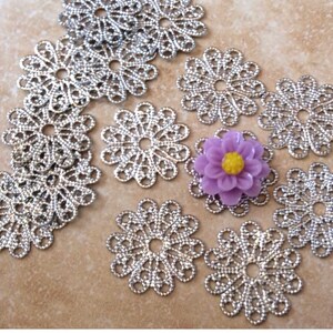 May include: A collection of silver filigree metal flower charms with a purple flower charm in the center.