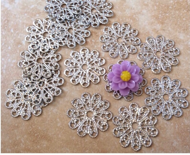 May include: A collection of silver filigree metal flower charms with a purple flower charm in the center.