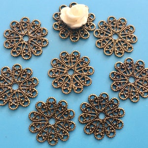 May include: Seven antique gold-toned metal filigree embellishments with a circular shape and a hole in the center. The embellishments have a delicate, intricate design.