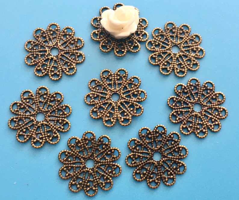 May include: Seven antique gold-toned metal filigree embellishments with a circular shape and a hole in the center. The embellishments have a delicate, intricate design.