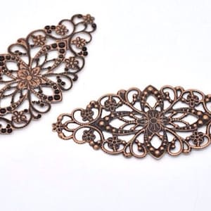 Peut inclure: Deux ornements en filigrane métallique ornés d'une finition cuivrée. Le filigrane est en forme de diamant et d'ovale. Le filigrane présente un motif floral avec de petites perles noires.