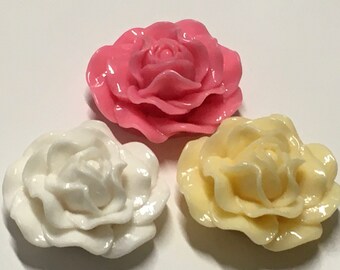 May include: Three resin rose embellishments in pink, white, and yellow. The roses have detailed petals and a glossy finish. These decorative flowers are suitable for crafts and embellishments.