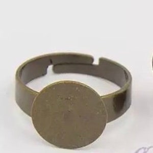 May include: A round, blank, metal ring base for jewelry making. The base is a light brown color and has a smooth, polished finish.