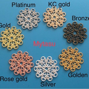May include: Assortment of eight decorative metal filigree charms in various colors, including platinum, gold, bronze, rose gold, and silver. The charms are arranged in a circle on a blue background. Mytasu is written in red text below the charms.