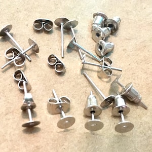 May include: A close-up of a group of silver earring backs. The backs are made of metal and have a variety of shapes and sizes.