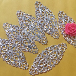 May include: Five silver filigree metal embellishments in the shape of a leaf with a pink flower in the center of one of the embellishments.