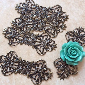 May include: Five antique brass filigree embellishments with a turquoise blue rose in the center. The filigree pieces have a floral design with intricate details.