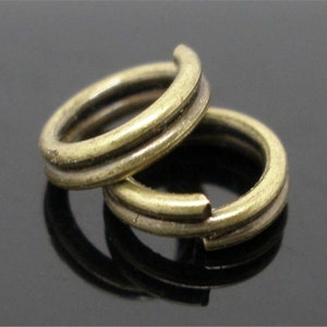 Puede incluir: Dos anillos de salto de metal de color dorado con un diseño de doble línea. Los anillos están apilados uno encima del otro.