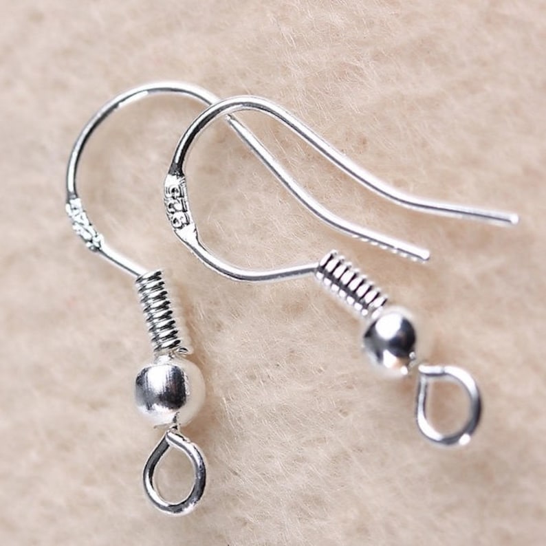 May include: A pair of silver earring hooks with a spring-loaded closure and a small ball at the end. The hooks are marked with "925" indicating they are made of sterling silver.