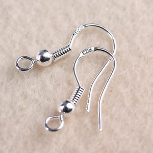 May include: Two silver earring hooks with a spring and a small ball at the top. The hooks are made of metal and are designed to be used with earrings.