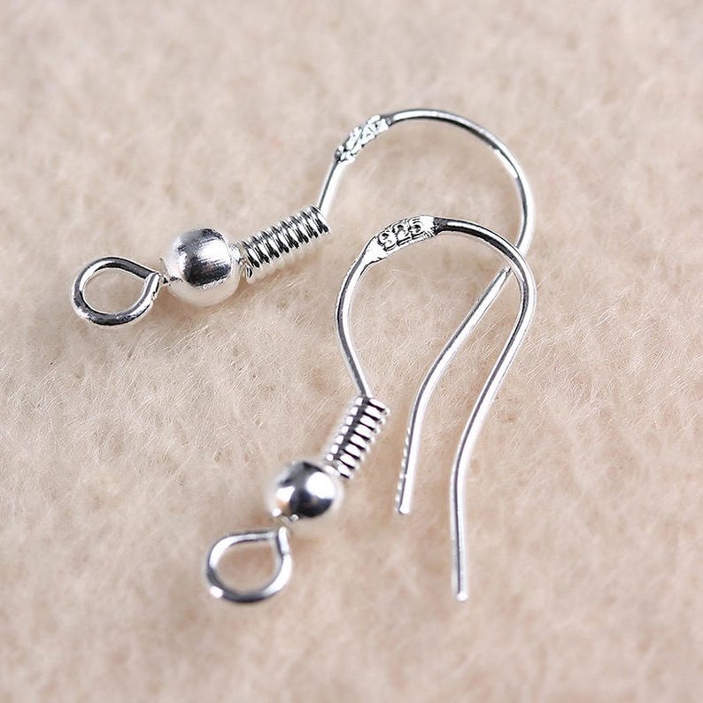 May include: Two silver earring hooks with a spring and a small ball at the top. The hooks are made of metal and are designed to be used with earrings.