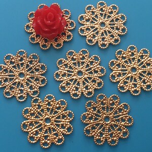 May include: Six gold-colored metal filigree embellishments with a circular design. The embellishments have a delicate, intricate pattern and a center hole.
