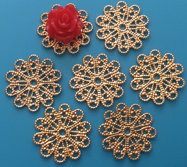 May include: Six gold-colored metal filigree embellishments with a circular design. The embellishments have a delicate, intricate pattern and a center hole.