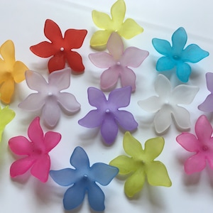 May include: Assortment of 13 plastic flower embellishments in various colours, including yellow, orange, red, pink, purple, blue, and white. Each flower has five petals and a centre hole.