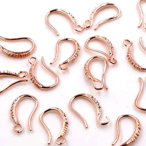 May include: A group of 12 rose gold earring hooks with a textured design. The hooks are made of metal and are designed for use in jewelry making.