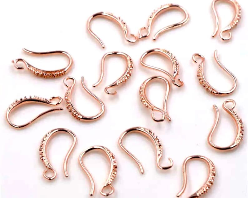 May include: A group of 12 rose gold earring hooks with a textured design. The hooks are made of metal and are designed for use in jewelry making.