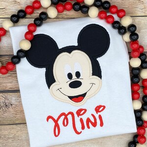 Puede incluir: Camiseta blanca con una imagen bordada de la cara de Mickey Mouse y la palabra "mini" en rojo.