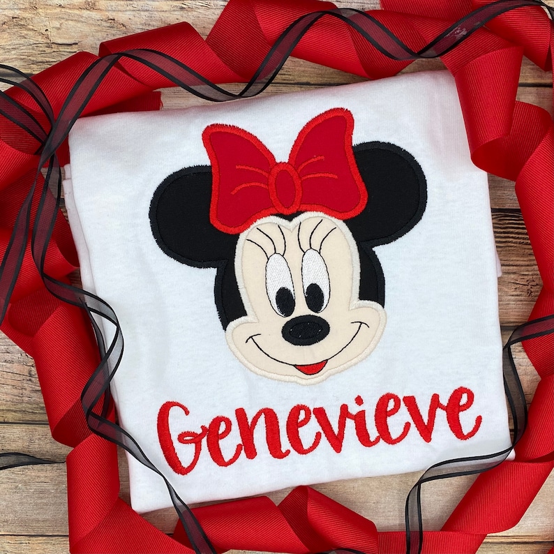 May include: White t-shirt with a red and black embroidered Minnie Mouse design and the name Genevieve in red embroidery.