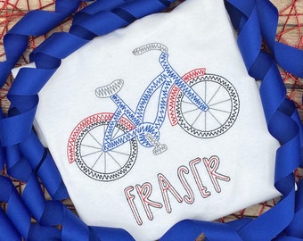 May include: White embroidered fabric with a blue and red bicycle design and the name "Fraser" stitched in red thread.