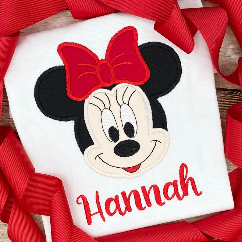 May include: White t-shirt with a red and black embroidered Minnie Mouse design and the name "Hannah" in red embroidery.