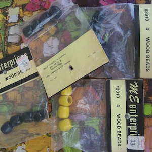 May include: Three packages of wooden beads, each containing four beads. The beads are black, yellow, and brown. The packages are labeled "ME Enterprises #3010 4 Wood Beads" and have a price tag of 39 cents.