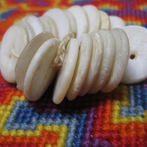 May include: A stack of white, round, smooth, and shiny mother of pearl buttons. The buttons are arranged in a circle and are stacked on top of each other.