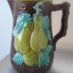 May include: A brown ceramic pitcher with a tree bark design and three yellow pears with green leaves.