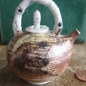 May include: A small, brown and white ceramic teapot with a white lid and a white handle. The teapot has a textured surface and a unique design.