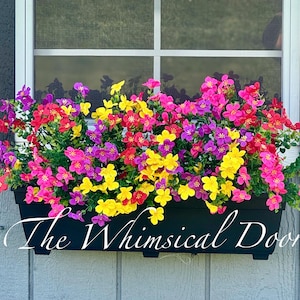 May include: A black window box overflowing with colorful faux flowers in shades of pink, yellow, red, and purple. The text "The Whimsical Door" is written in a cursive font across the bottom of the box.