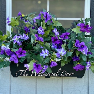 May include: A black window box overflowing with vibrant purple and white petunias and green ivy. The flowers are in full bloom, creating a lush, colorful display. The text "The Whimsical Door" is written on the window box.