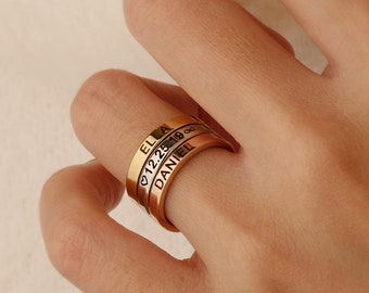 May include: A rose gold personalized ring with three bands. Each band is engraved with a name and a date. The ring is worn on a finger. The text on the ring includes the names "ELLA" and "DANIEL".