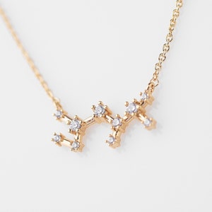 Peut inclure: Un collier en or avec un pendentif en forme de constellation orné de petites pierres claires. Le pendentif représente la constellation du Sagittaire.