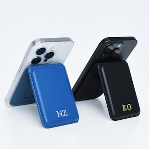 May include: Two smartphones propped up by matching magnetic phone wallets. One phone is silver, the other black. The wallets are blue and black, each with gold initials. The blue wallet has "NZ" and the black wallet has "KG".