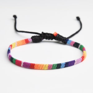 May include: A colourful woven friendship bracelet with a rainbow pattern and black adjustable closure.