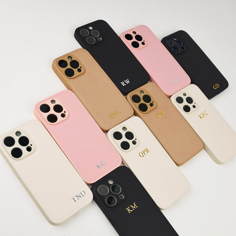 May include: A collection of ten smartphone cases in black, tan, pink, and cream colours. Each case features a triple-lens camera cutout and is personalised with two or three gold or silver embossed letters, including RW, RD, GD, BMC, KM, KFC, KG, QPR, TND, and KM.