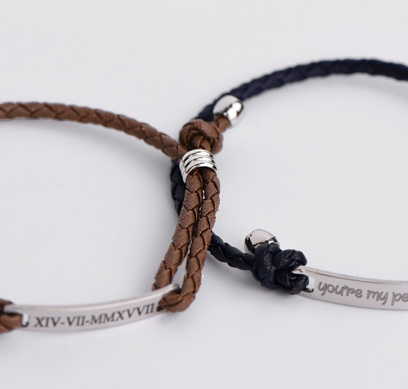May include: Two braided leather bracelets with silver metal accents. One bracelet has the inscription "XIV-VII-MMXVII" and the other has the inscription "You're my person".