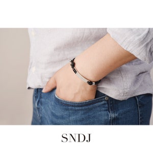 May include: A black braided bracelet with a silver bar that says "SNJD" on it.