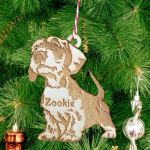 May include: A wooden Christmas ornament shaped like a dog with the name "Zookie" engraved on its chest. The ornament is hanging on a Christmas tree.