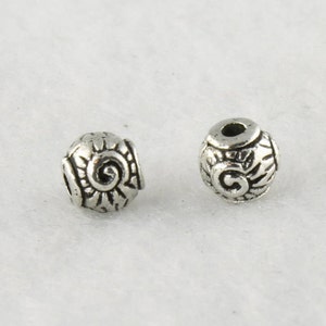 Puede incluir: Dos cuentas de metal plateado con un dise&ntilde;o de espiral. Las cuentas son redondas y tienen un agujero en el centro.