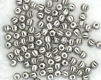 May include: A pile of silver metal beads with a ridged design. The beads are small and round, and they are perfect for jewelry making.