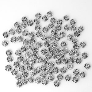 May include: A large quantity of silver-toned metal beads with a twisted design. The beads are scattered on a white surface.